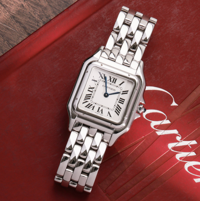A silver watch on a red surfaceDescription automatically generated